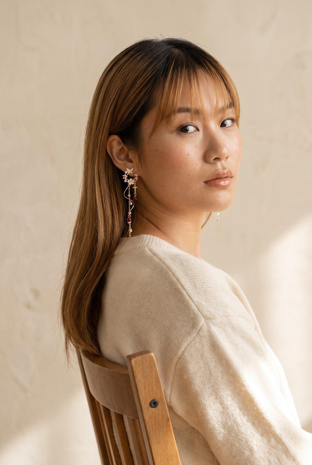 A model seated on a wooden chair wearing the Starfall Earrings